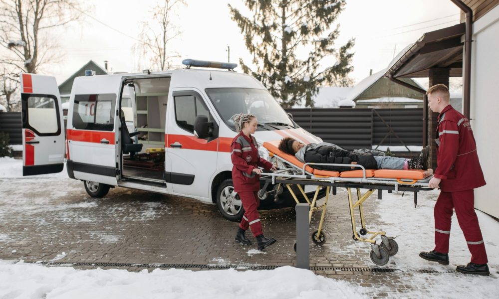 Paramedics transporting a patient on a stretcher to an ambulance on a snowy day.